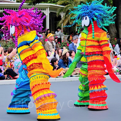 花や鳥モチーフの衣装のダンサーたちの後ろを歩く モメラス